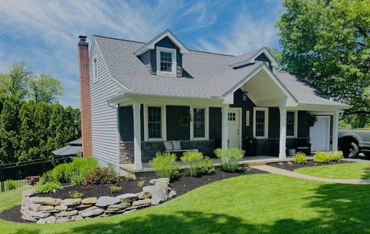Exterior angled view of cape cod new gray siding, blue vinyl shakes, dry stacked stone, and white window trim.